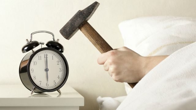 Hand with Hammer Smashing Alarm Clock from Bed